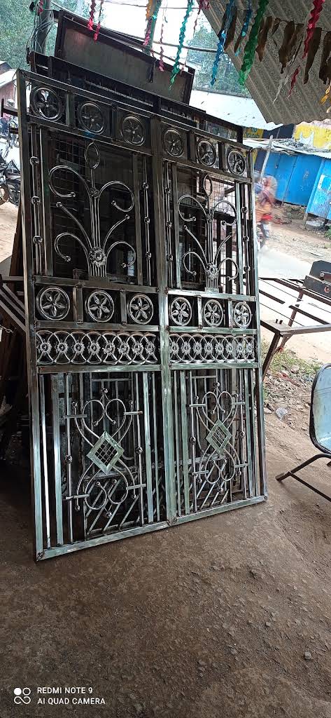 Ornamental steel gate with floral scroll designs and decorative wheel motifs crafted by Hanuman Fabrication
